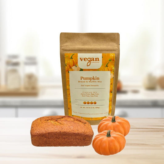 A packaged vegan pumpkin bread/muffin mix with a small loaf of pumpkin bread and two small pumpkins in the foreground on a kitchen counter.